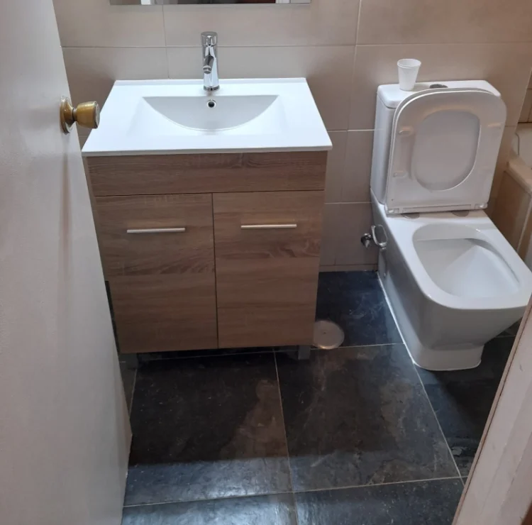 Baño reformado en el barrio de Salamanca: lavabo sobre mueble suspendido de madera, grifería cromada, inodoro y suelo de pizarra
