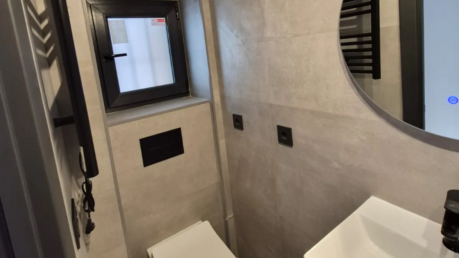 Baño terminado en una reforma integral en Usera: porcelánico de gran formato, inodoro suspendido con cisterna empotrada y grifería negra