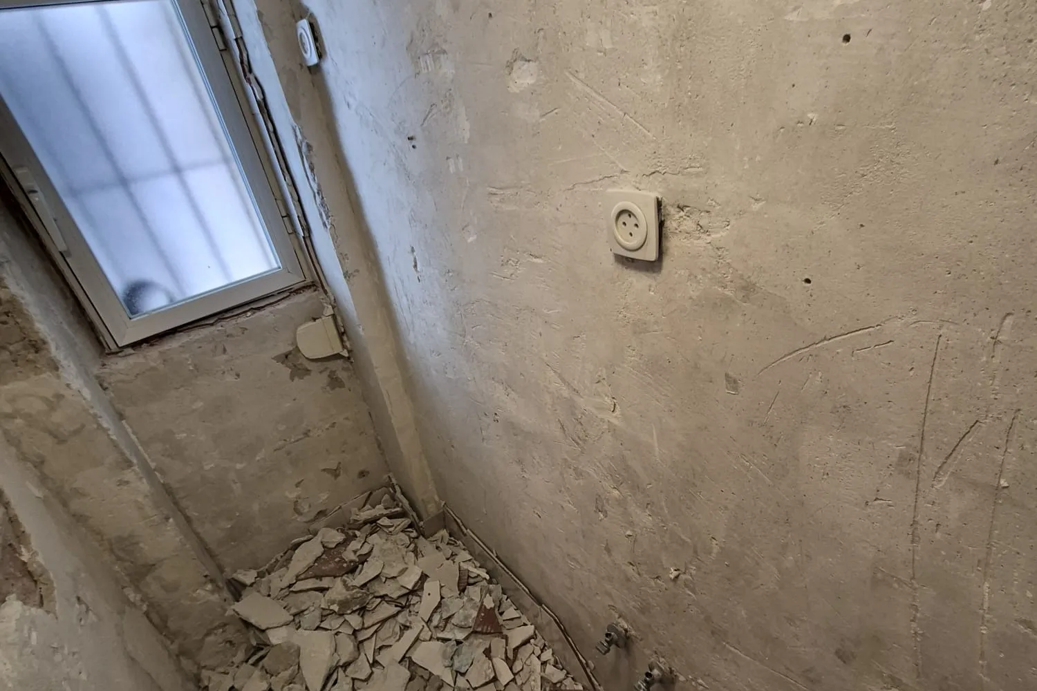 Baño de un piso de Usera picado, con el alicatado retirado y la fontanería antigua de hierro a la vista