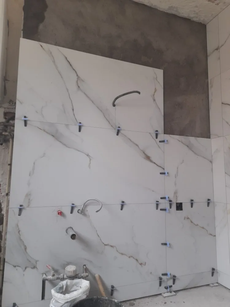 Porcelánico de gran formato imitación mármol durante la colocación, con crucetas de nivelación y las tomas de fontanería preparadas detrás